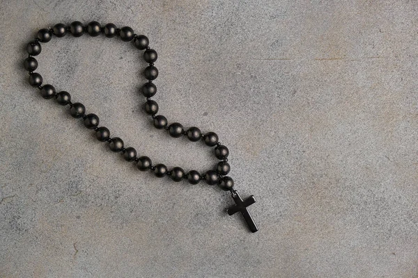 Black obsidian rosary with a cross on an abstract gray background. Christian rosary beads. Top view. Selective focus. Space for lettering and design