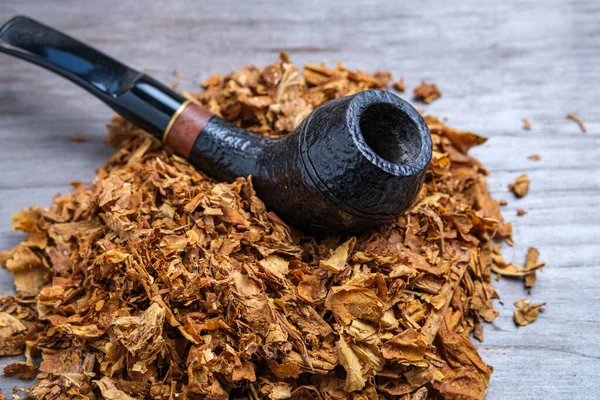 Black curved pipe and tobacco on a wooden background. Close-up. Selective focus.
