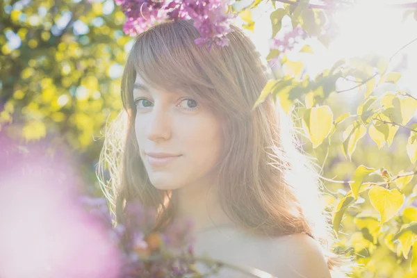 Aantrekkelijke vrouw op zoek naar de camera onder bloeiende tuin. — Stockfoto