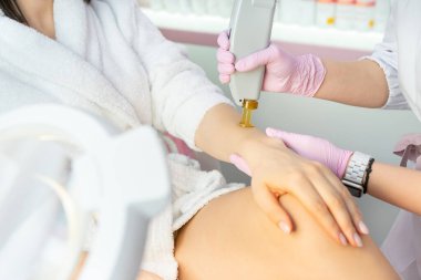 Profesyonel vücut bakım kliniğinde El 'in lazer tüy çıkarma prosedürü. Elleri pembe eldivenli, ellerinde saç çıkarma makinesi aletleri var. Modern lüks kozmetik epilasyon hizmeti Beyaz ve pembe renkler