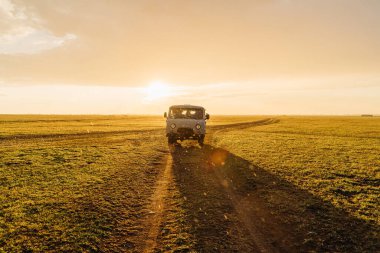 Macera ruhu. Eski bir Sovyet off-road aracı olan UAZ, bir kır yolunda otobüs turu yapıyor. Sıcak, güzel bir gün batımı sepya ışığı ve yağmur. Arka ışık. Romantik nostaljik film sinematik yatay fotoğraf