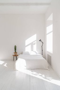 Temiz ve şık beyaz yatak odasının içinde güneşli bir sabah. Tahta masada duran kaktüs ve diğer tarafta siyah lamba. Boş beyaz kopya alanı. Temel tasarım. Kırsal ya da İskandinav tarzı. Dikey 