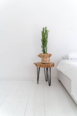 Beyaz yatak odasının içi temiz ve şık. Dikey minimalist kompozisyon ve kaktüs ayakta duran ahşap masa. Boş beyaz kopya alanı. Kırsal ya da İskandinav tarzı. yatak, yastık ve temiz çarşaflar