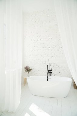Banyo penceresinden güneş ışınları geliyor. Mutlu yaz sabahları. Beyaz şık minimalist banyo şeffaf perdeler ve tuğla duvarla kaplı. Dikey kompozisyon. İç mimari tasarım. 
