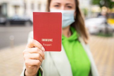Dokunulmaz sağlık pasaportu. Kırmızı aşı sertifikası taşıyan maskeli sarışın Avrupalı kadın. Covid pandemik seyahat ve kamu kısıtlaması teması. Yatay fotoğraf. Yeşil günlük kıyafetler.
