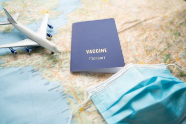 Aşılanmış gezgin uçak biletleri ve seyahat planları yapıyor. Mavi aşı pasaportlu masa, harita, uçak ve koruyucu yüz maskesi. Covid pandemik kısıtlamalar sırasında seyahat etmek güvenlik kuralları