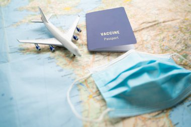 Aşı pasaportu mavi sertifika. Kırmızı tırnaklı bir kadın elinde mavi bir belge tutuyor. Salgın covid kısıtlamaları sırasında seyahat etmek. Masada harita, uçak ve yüz maskesi olan yatay bileşim