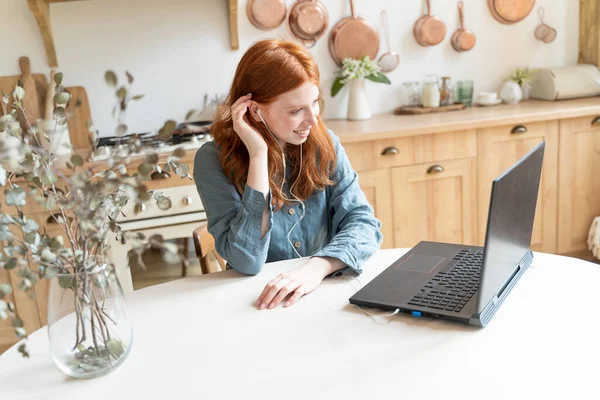 快乐的红头发女人在厨房用笔记本电脑在线视频通话 红头发的白人女人在网上开会时面带微笑地享受着谈话 长距离关系 待在家里 — 图库照片