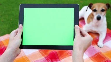 Piknik halı ile sevimli köpek oturan tablet bilgisayar kullanan kız