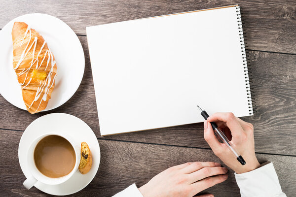 Стол с блокнотами, чашкой кофе и круассаном
