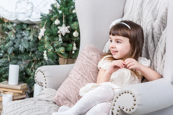 Felice bambina si siede comodamente in una sedia domestica beige chiaro . — Foto Stock