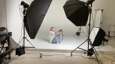 Profesyonel fotoğraf stüdyosunda yerde oturan kadın fotoğrafçı kamerayla selfie çekiyor ve küçük sevimli köpeği Jack Russell terrier ile oynuyor. profesyonel fotoğraf ekipmanları yanıp sönüyor