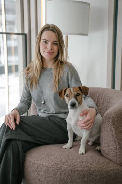 Sarı kadın ve köpek Jack Russell Terrier pembe sandalyede oturmuş kameraya bakıyor. Doğal ışık. dikey bileşim