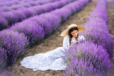 Büyük şapkalı ve uzun elbiseli güzel bir kız lavanta toplar. Yazın fotoğrafı..