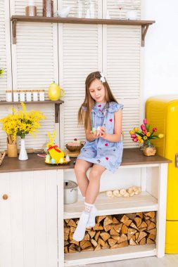 Mutlu Paskalyalar. Çocuk Paskalya için hazırlanıyor. Bir kız dekore edilmiş bir mutfakta oturuyor ve elinde Paskalya yumurtası tutuyor..