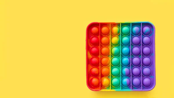 New popular silicone colorful antistress pop it toy for child on yellow background. View from above. Copy space. Simple dimple.