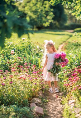 Büyük bir buket şakayıklı küçük kız. Yazın elinde çiçeklerle parkta yürüyen bir çocuk...