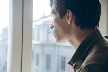 Young sad man looking out the window clipart