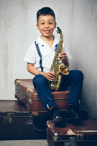 Six years old boy sit with saxophone on retro suitcases — Stock Photo, Image