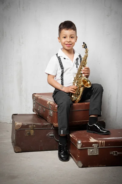 Six years old boy sit with saxophone on retro suitcases — Stock Photo, Image