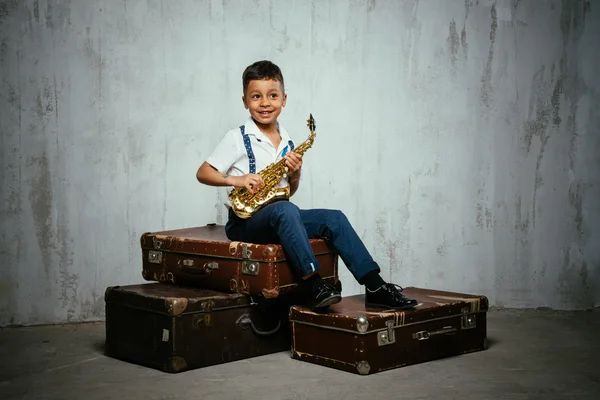 Six years old boy sit with saxophone on retro suitcases — Stock Photo, Image