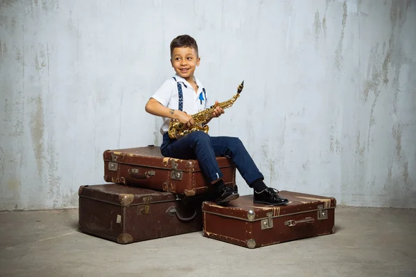 Six years old boy sit with saxophone on retro suitcases — Stock Photo, Image