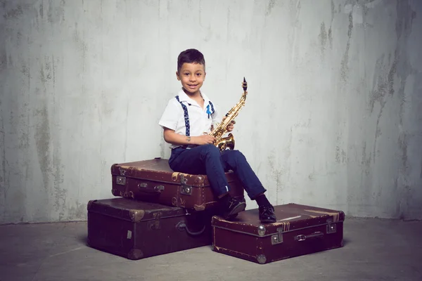 Six years old boy sit with saxophone on retro suitcases — Stock Photo, Image