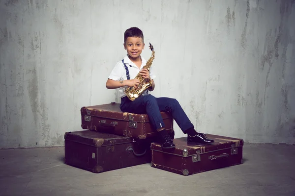 Six years old boy sit with saxophone on retro suitcases — Stock Photo, Image