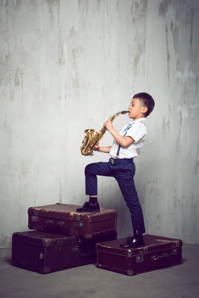 Niño de seis años de edad de pie en siuitcases retro y jugar saxo —  Fotos de Stock