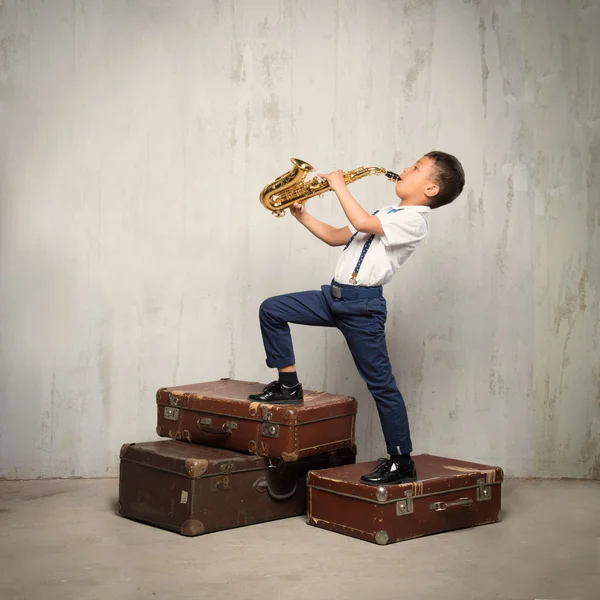 Six years old boy stand on retro siuitcases and play sax — Stock Photo, Image
