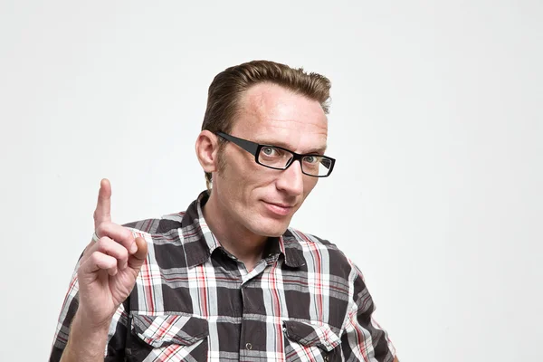 Handsome man in eyeglasses and tartan shirt put his index finger up. — Stock Photo, Image