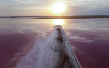 Pembe bir gölde parlak bir gün batımı, plajın pembe sularında turuncu bir alev..
