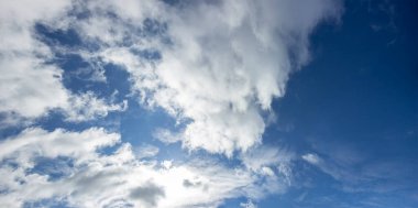 Mavi gökyüzündeki beyaz bulutlar ve bulutların arkasındaki parlak güneş..