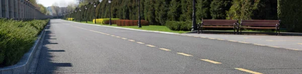 Asphalt road with yellow markings along a high fence and plants that sit along the road