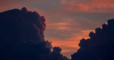 Kırmızı günbatımından aydınlanan ve bulutların arkasına saklanan koyu renkli yoğun bulutlar arasında dramatik turuncu gökyüzü.