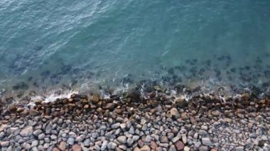Taşlarla kıyıda mavi denizin dalgalarını yıkıyor..