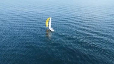 Sarı ve beyaz yelkenli küçük bir yelkenli mavi denizde yelken açar.