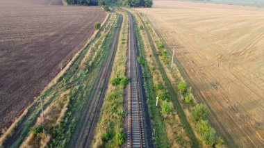 Tarlalardan ve ormanlardan geçen demiryolu. Toprak yolda küçük bir araba.