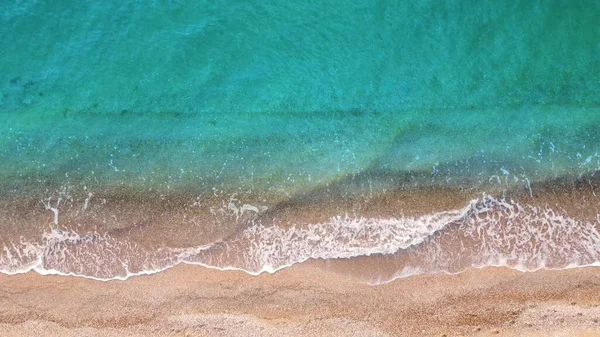 Top view on the waves of turquoise and clear sea water washing the sand on the shore. Summer warm sand and rest by the sea