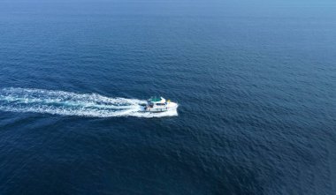 Turistlerin açık mavi denizde yelken açtığı küçük bir teknenin havadan görüntüsü.