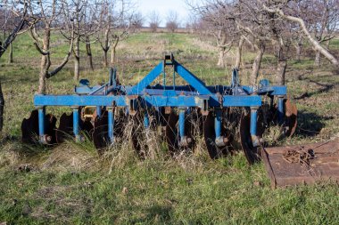 Mavi disk harrow ağaçların arasında uzun otlar arasında dinlenen, paslı bıçaklar, mevsimsel tarım ve çiftlik terk göstermektedir