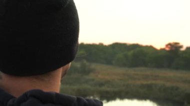 Yakın plan. Sporcu kenara yaklaşıyor, göle bakıyor, kırsal kesimdeki ağaçlara bakıyor.