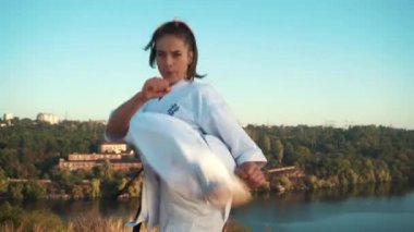 Genç kadın beyaz kimono karate tekniğini sahne arkasına karşı gösteriyor.