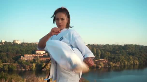 Młoda kobieta białe kimono demonstruje swoją technikę karate na tle natury — Wideo stockowe