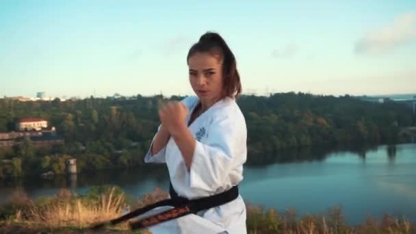 Tłumaczenie: "Kyokushinkai". młoda kobieta biały kimono demonstruje karate technika na tle natury — Wideo stockowe