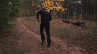 Siyah elbiseli bir adam antrenman yapıyor, çam ağaçları arasında koşuyor, sonbahar.