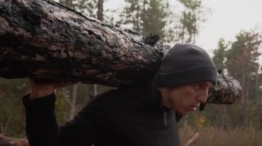 Kaslı sporcu ağır yük kaldırıyor, ormanda kütük tutuyor. Sonbaharda