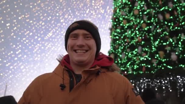 Lächelnder Kerl auf einem kleinen städtischen Weihnachtsbaum auf dem Platz, im neuen Jahr, Weihnachten. Pandämonium der Menschen — Stockvideo