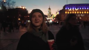The girl drinks coffee on the background of the city, cars, lanterns, people