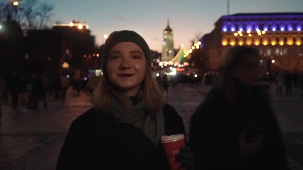 The girl drinks coffee on the background of the city, cars, lanterns, people — Stockvideo